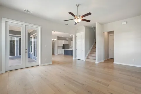 a view of an empty room with wooden floor and a ceiling fan