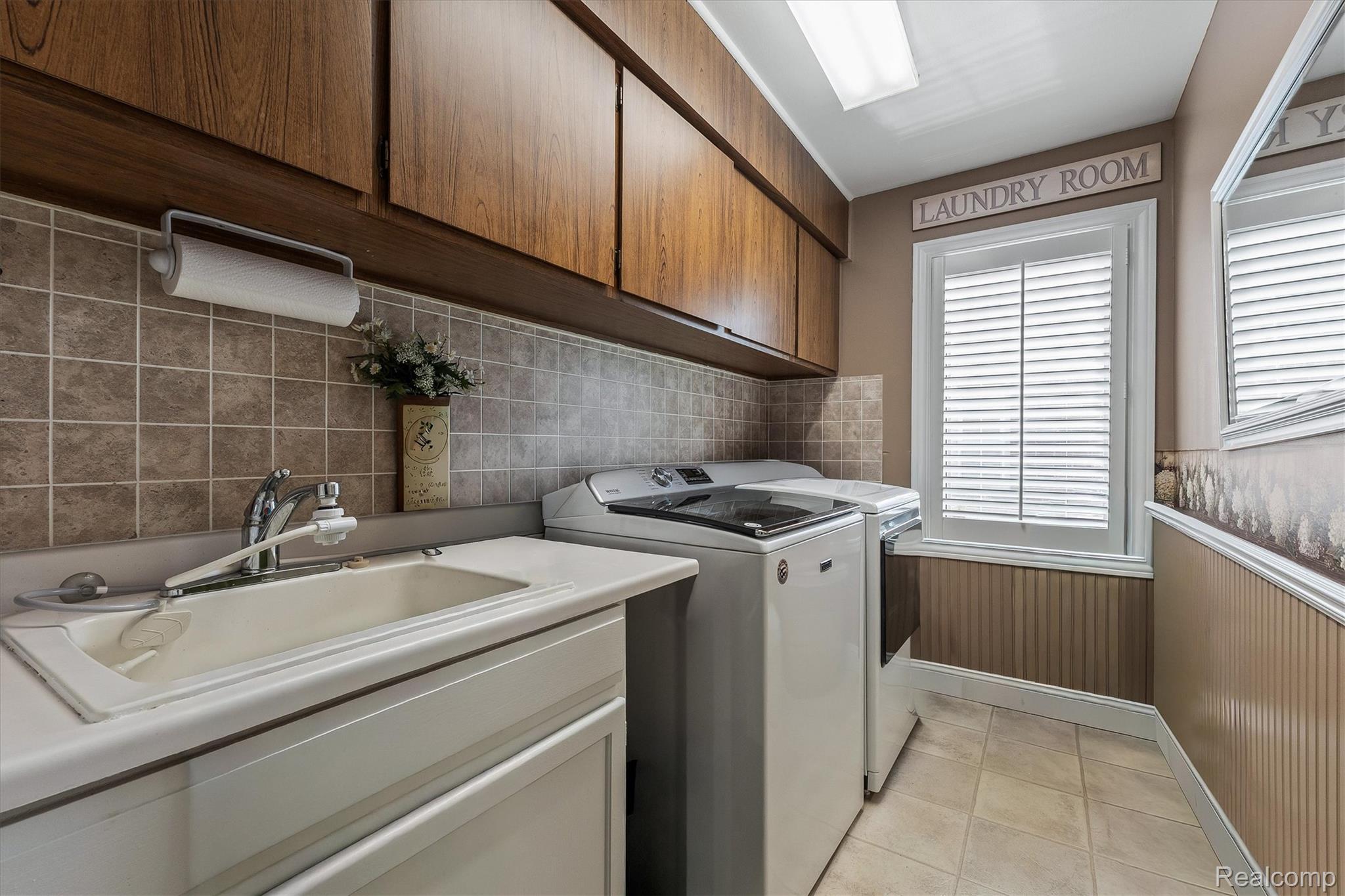 1662 Sumac Drive Rochester, MI 48309 - Photo 19 of 38 Dedicated laundry area featuring a utility sink, wood-finish cabinetry, tile backsplash, plantation shutters, and beadboard paneling