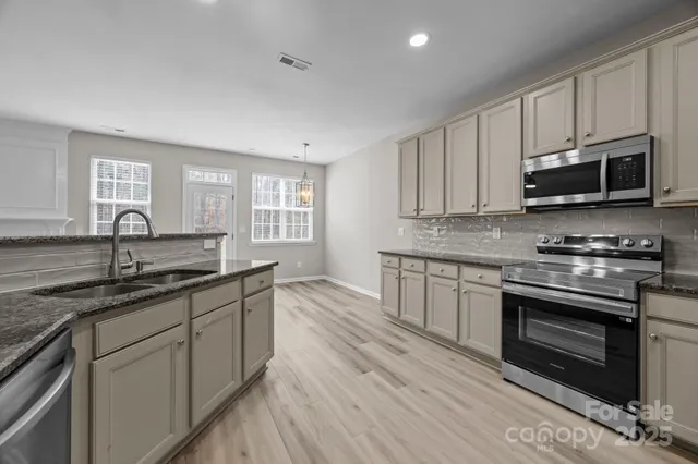 a kitchen with kitchen island granite countertop wooden cabinets a sink a stove a refrigerator and dishwasher with wooden floor