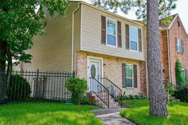 a view of a house with brick walls and a yard with a large tree