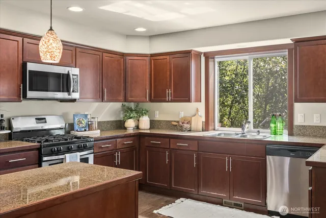 a kitchen with kitchen island granite countertop a sink stainless steel appliances wooden cabinets and a window