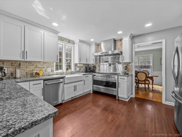 a kitchen with stainless steel appliances granite countertop a refrigerator a stove top oven a sink dishwasher and white cabinets with wooden floor