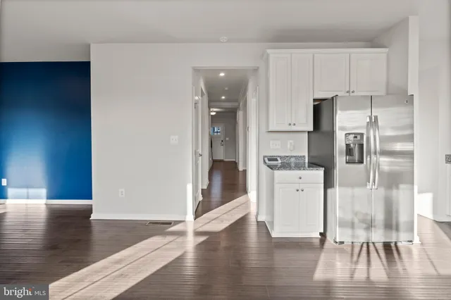 a open kitchen with stainless steel appliances granite countertop a stove top oven a refrigerator a sink and white cabinets with wooden floor