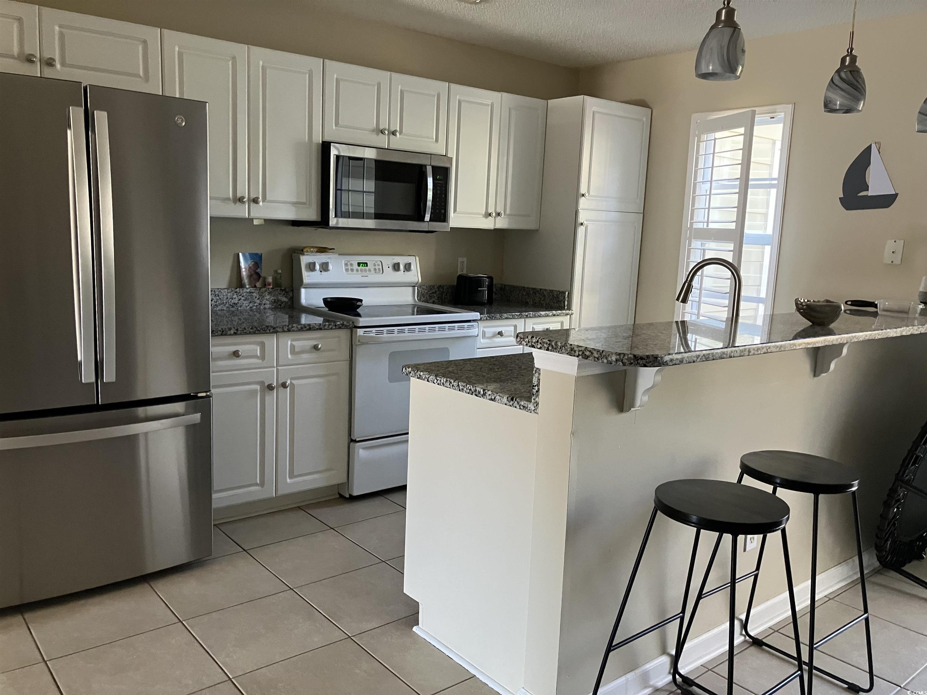 4840 Moss Creek Loop, Unit 31 Murrells Inlet, SC 29576 - Photo 7 of 24 Kitchen featuring appliances with stainless steel finishes, light tile patterned flooring, white cabinets, a kitchen bar, and hanging light fixtures