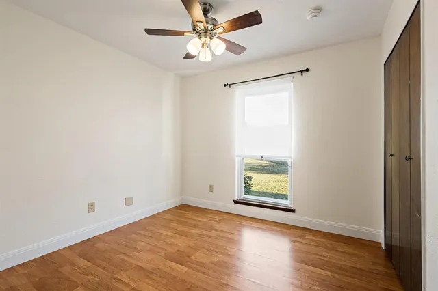 an empty room with wooden floor chandelier fan and windows