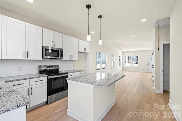 a kitchen with stainless steel appliances granite countertop a stove a sink dishwasher a refrigerator white cabinets and wooden floor next to a window