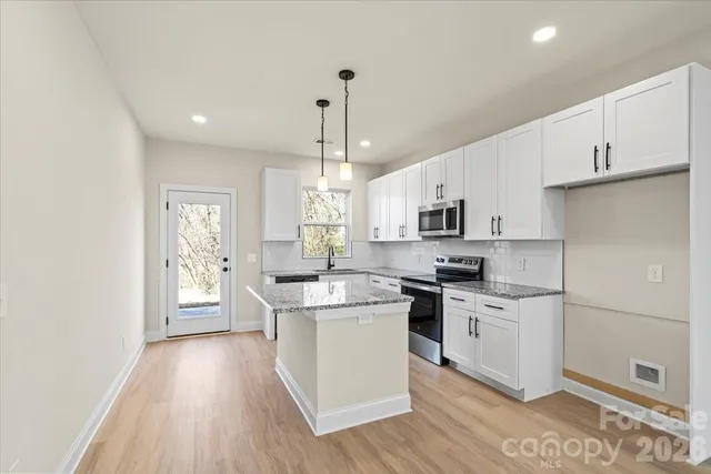 a kitchen with stainless steel appliances granite countertop a stove a sink dishwasher a refrigerator white cabinets and wooden floor