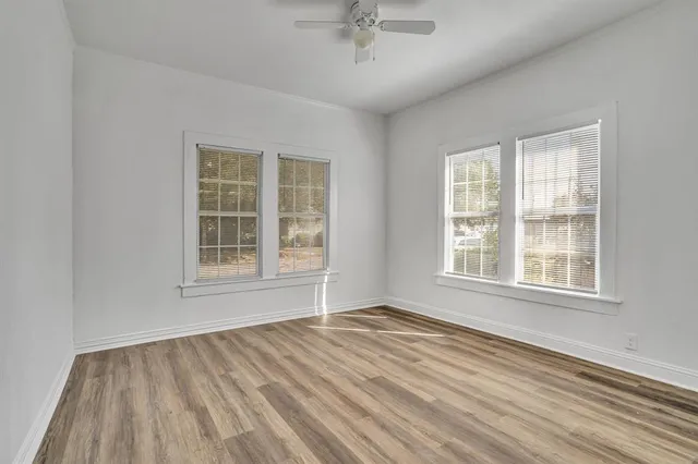 an empty room with wooden floor fan and windows