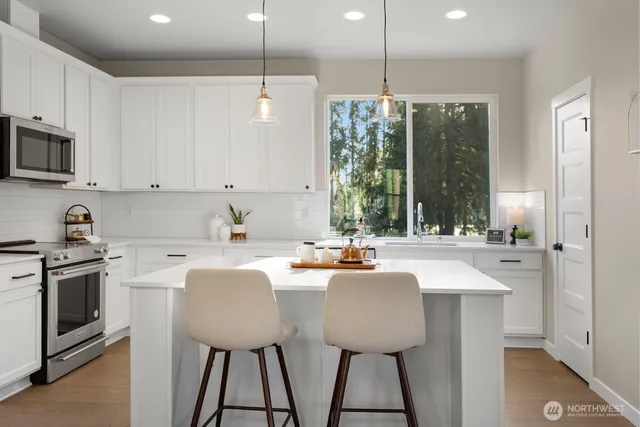 a kitchen with stainless steel appliances granite countertop a stove a sink a microwave a refrigerator white cabinets and wooden floor