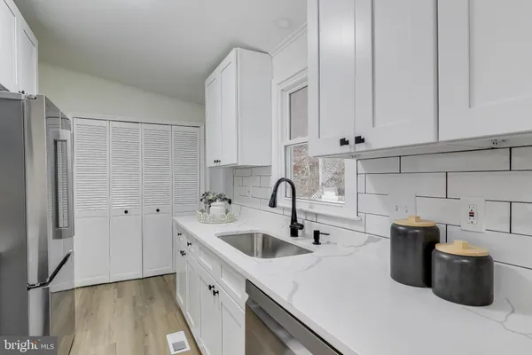 a kitchen with a sink dishwasher and white cabinets with wooden floor