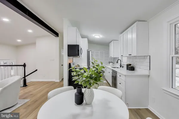 a white kitchen with stainless steel appliances a white table a potted plant and a wooden floor