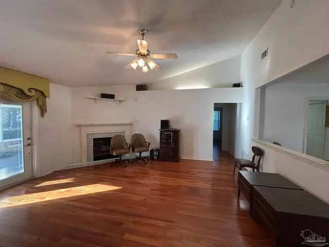a view of a livingroom with a fireplace a ceiling fan and wooden floor