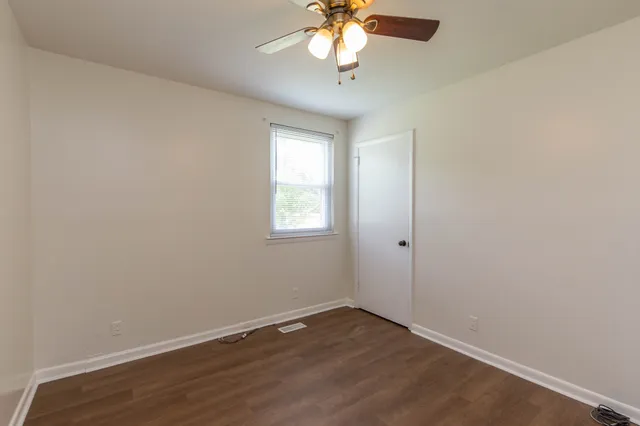an empty room with wooden floor chandelier fan and windows