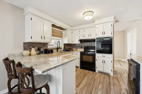a kitchen with stainless steel appliances granite countertop a stove a refrigerator a sink dishwasher and white cabinets with wooden floor