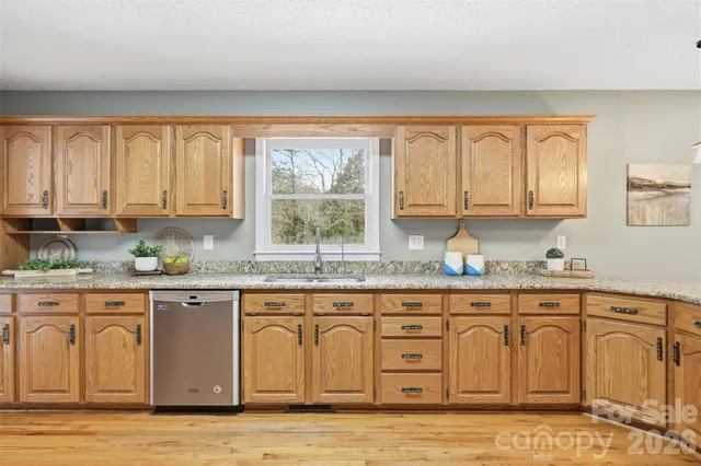 a kitchen with granite countertop a stove a sink and white cabinets with wooden floors