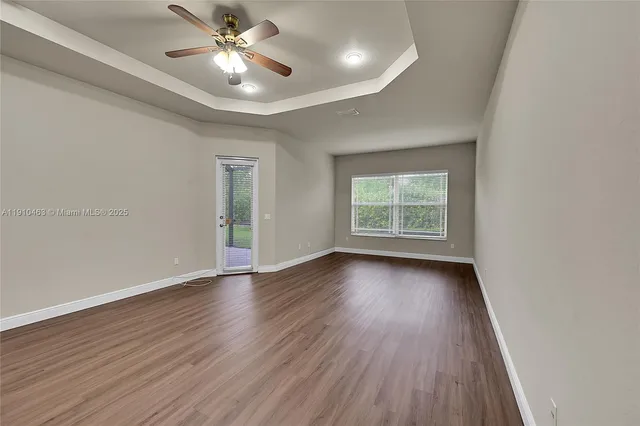 an empty room with wooden floor chandelier fan and windows