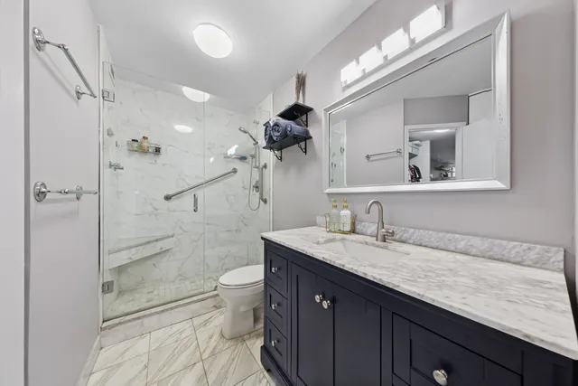 a bathroom with a granite countertop sink a toilet a mirror and shower