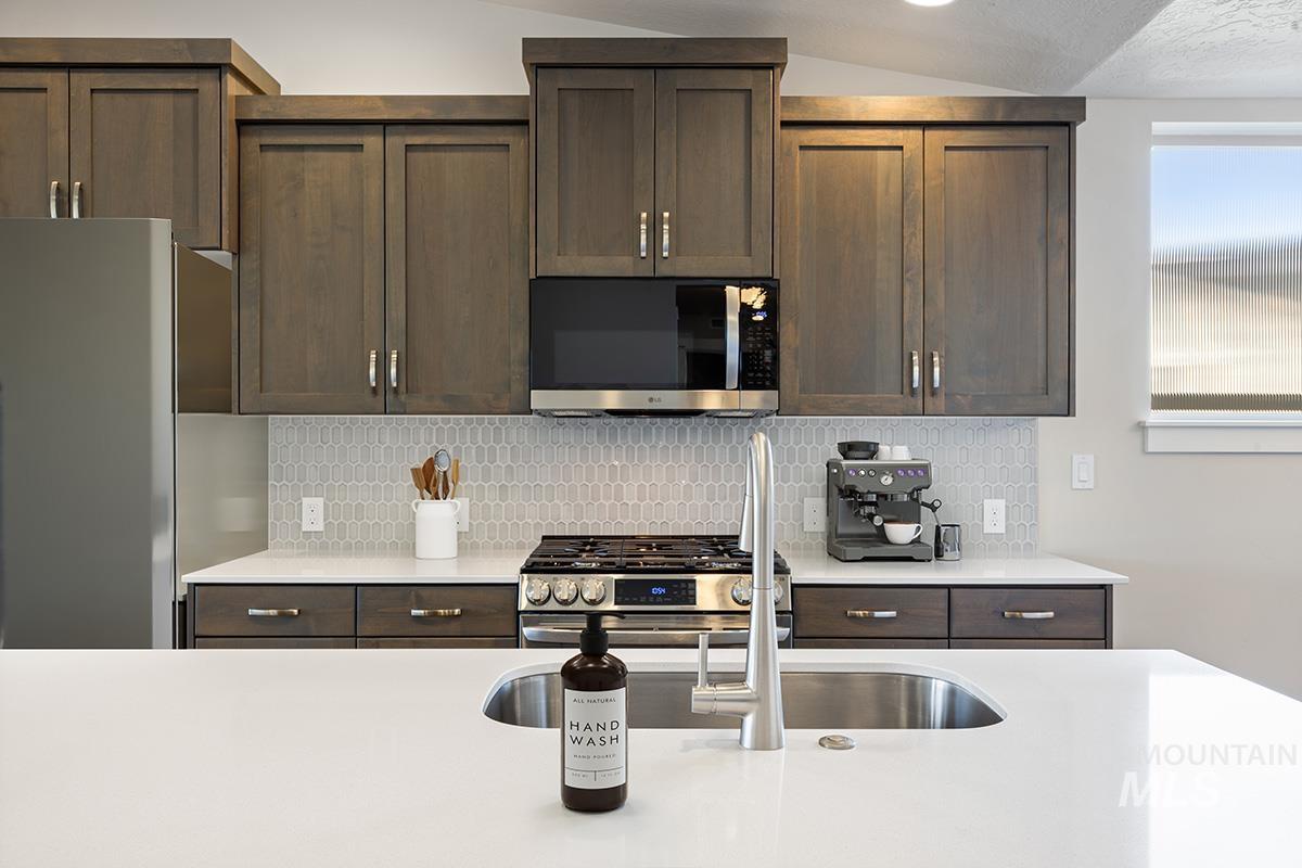 283 West Norwich Street Meridian, ID 83642 - Photo 8 of 25 Kitchen with appliances with stainless steel finishes, dark brown cabinets, backsplash, and a textured ceiling