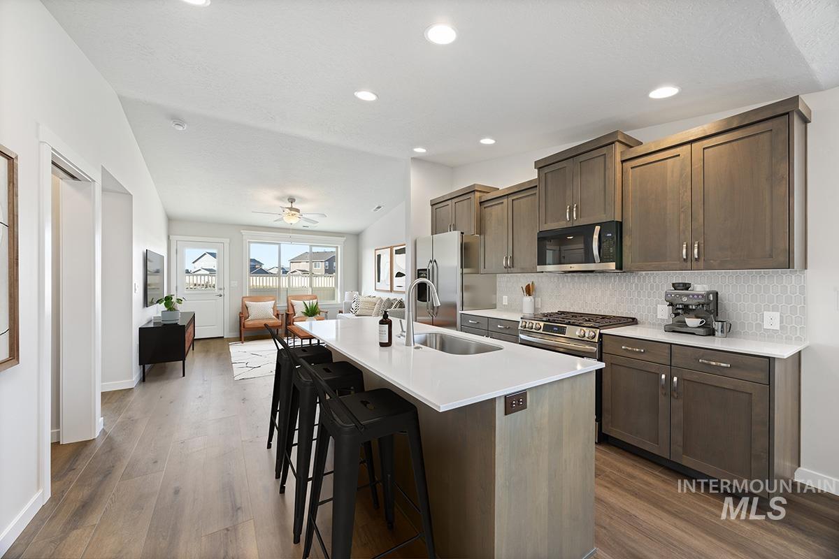 283 West Norwich Street Meridian, ID 83642 - Photo 9 of 25 Kitchen with dark brown cabinetry, an island with sink, a breakfast bar area, appliances with stainless steel finishes, and recessed lighting