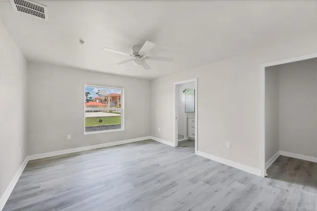 an empty room with wooden floor fan and windows