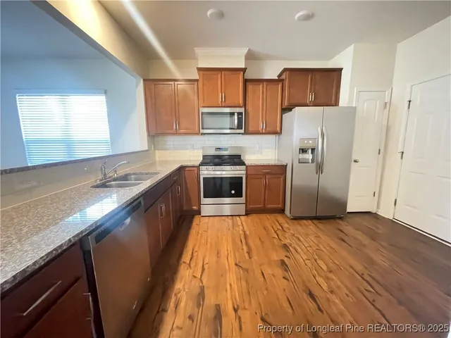 a kitchen with stainless steel appliances granite countertop a refrigerator a sink dishwasher a stove with wooden floor and cabinets