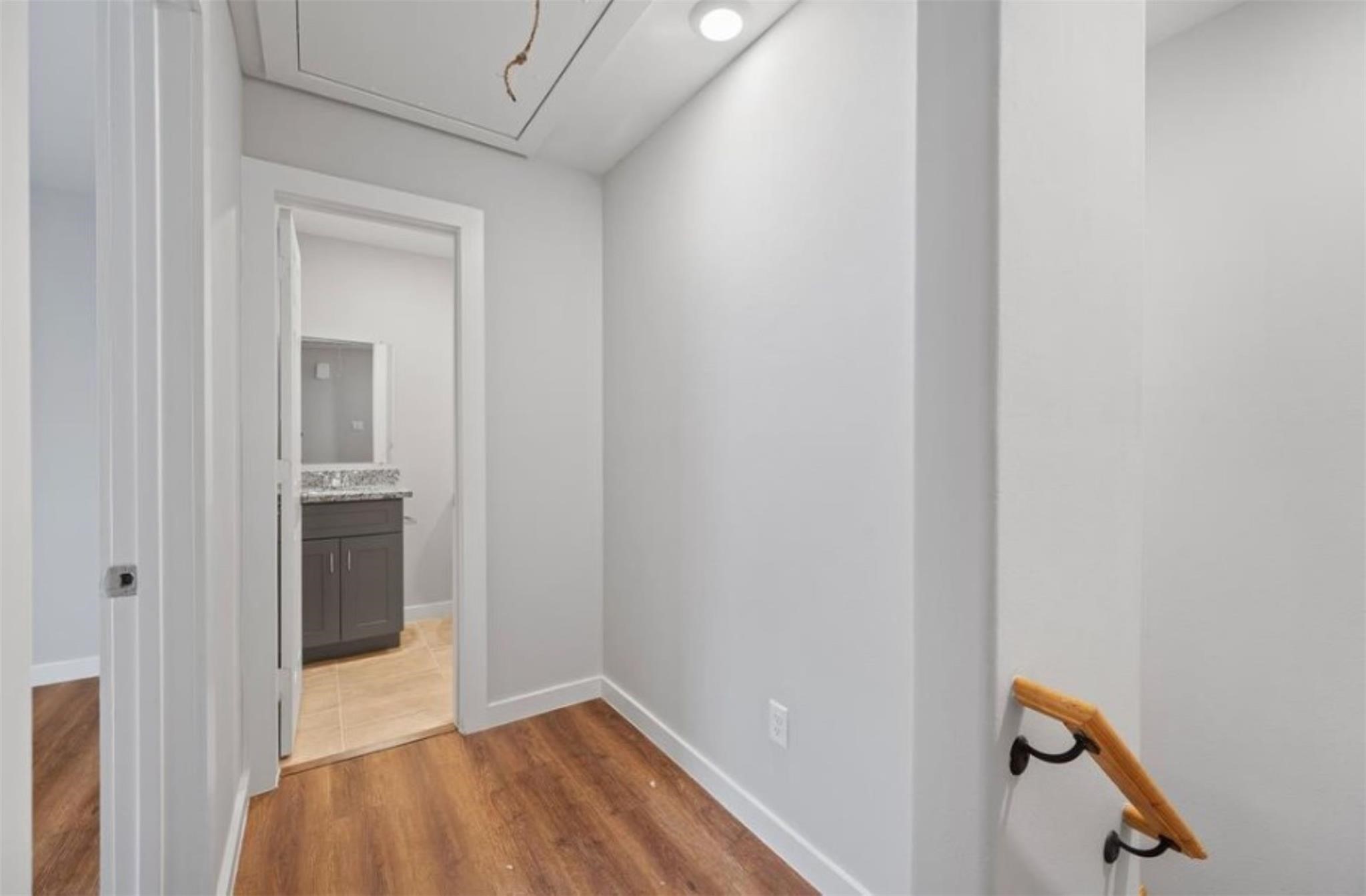 8120 Laura Koppe Road, Unit B Houston, TX 77028 - Photo 2 of 25 This photo shows a small hallway with light-colored walls and wood flooring, leading to a bathroom with a granite countertop and dark cabinetry. A staircase with a wooden handrail is visible on the right.