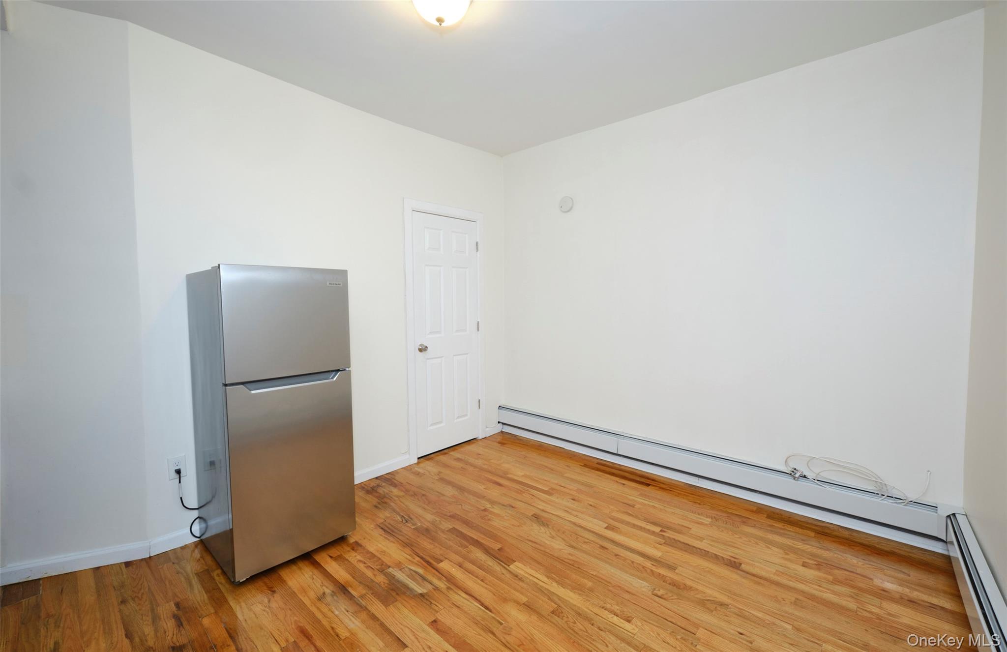 563 Miller Avenue Brooklyn, NY 11207 - Photo 11 of 21 Empty room featuring a baseboard heating unit, light wood-style flooring, and a baseboard radiator