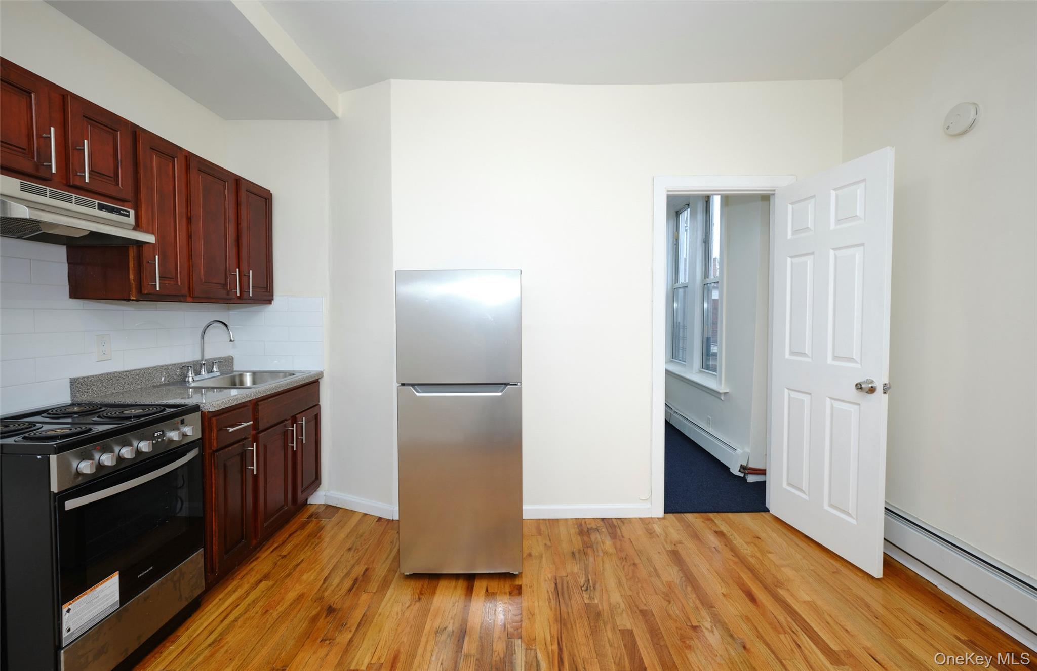 563 Miller Avenue Brooklyn, NY 11207 - Photo 5 of 21 Kitchen with appliances with stainless steel finishes, baseboard heating, under cabinet range hood, and backsplash