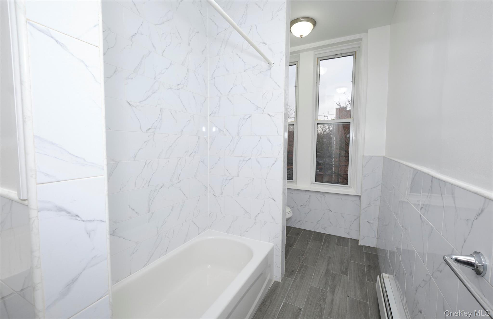 563 Miller Avenue Brooklyn, NY 11207 - Photo 6 of 21 Bathroom with tile walls, a baseboard radiator, a wainscoted wall, and a combined bath / shower with marble appearance