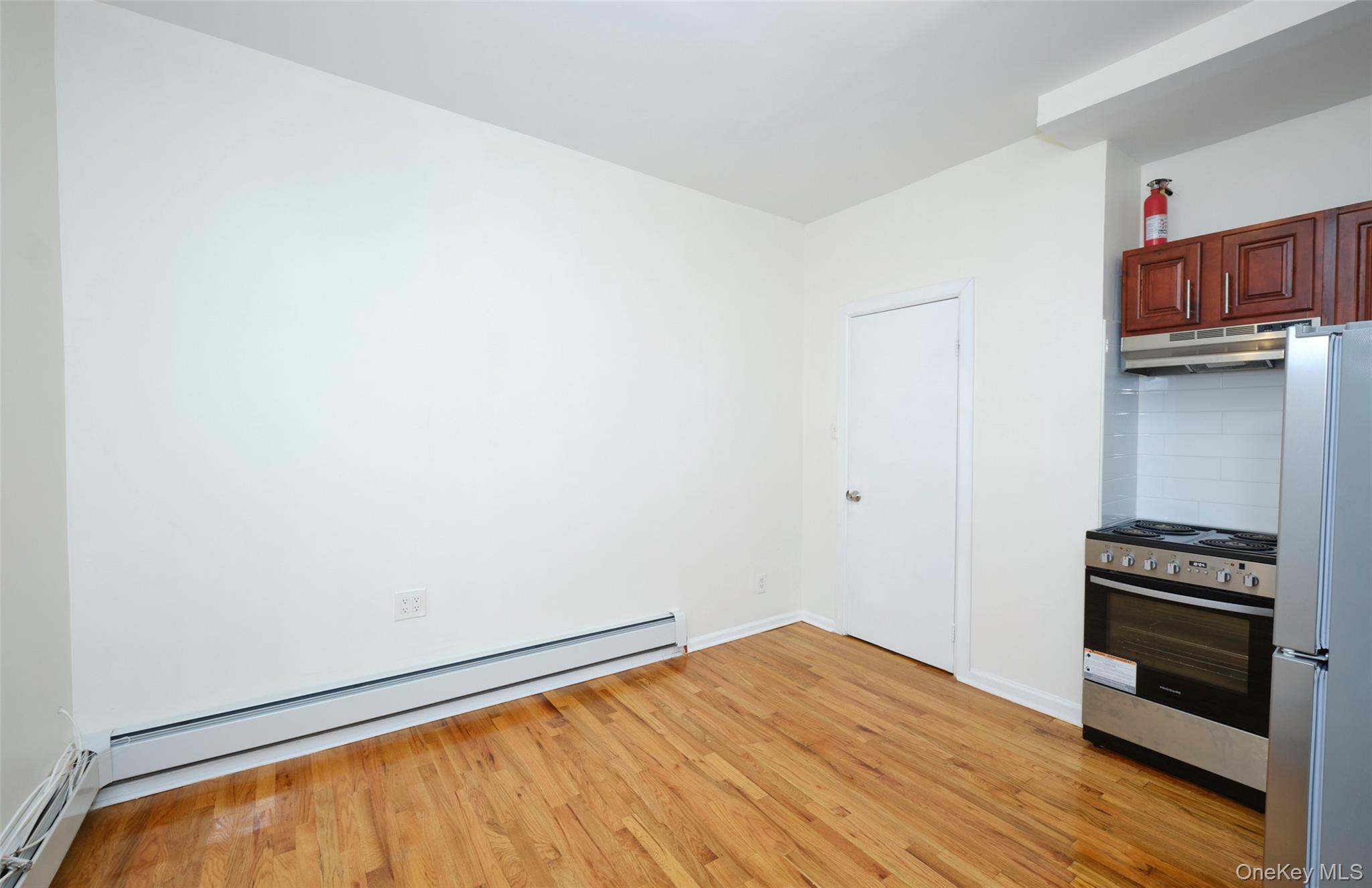 563 Miller Avenue Brooklyn, NY 11207 - Photo 10 of 21 Kitchen with stainless steel appliances, a baseboard radiator, light wood-type flooring, and under cabinet range hood