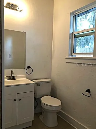 a bathroom with a granite countertop toilet a sink a mirror and a window
