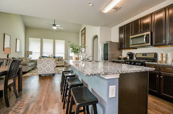a kitchen with stainless steel appliances granite countertop a stove top oven a sink dishwasher a dining table and chairs with wooden floor