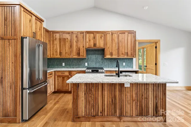 a kitchen with stainless steel appliances granite countertop a refrigerator a sink dishwasher and wooden cabinets with wooden floor