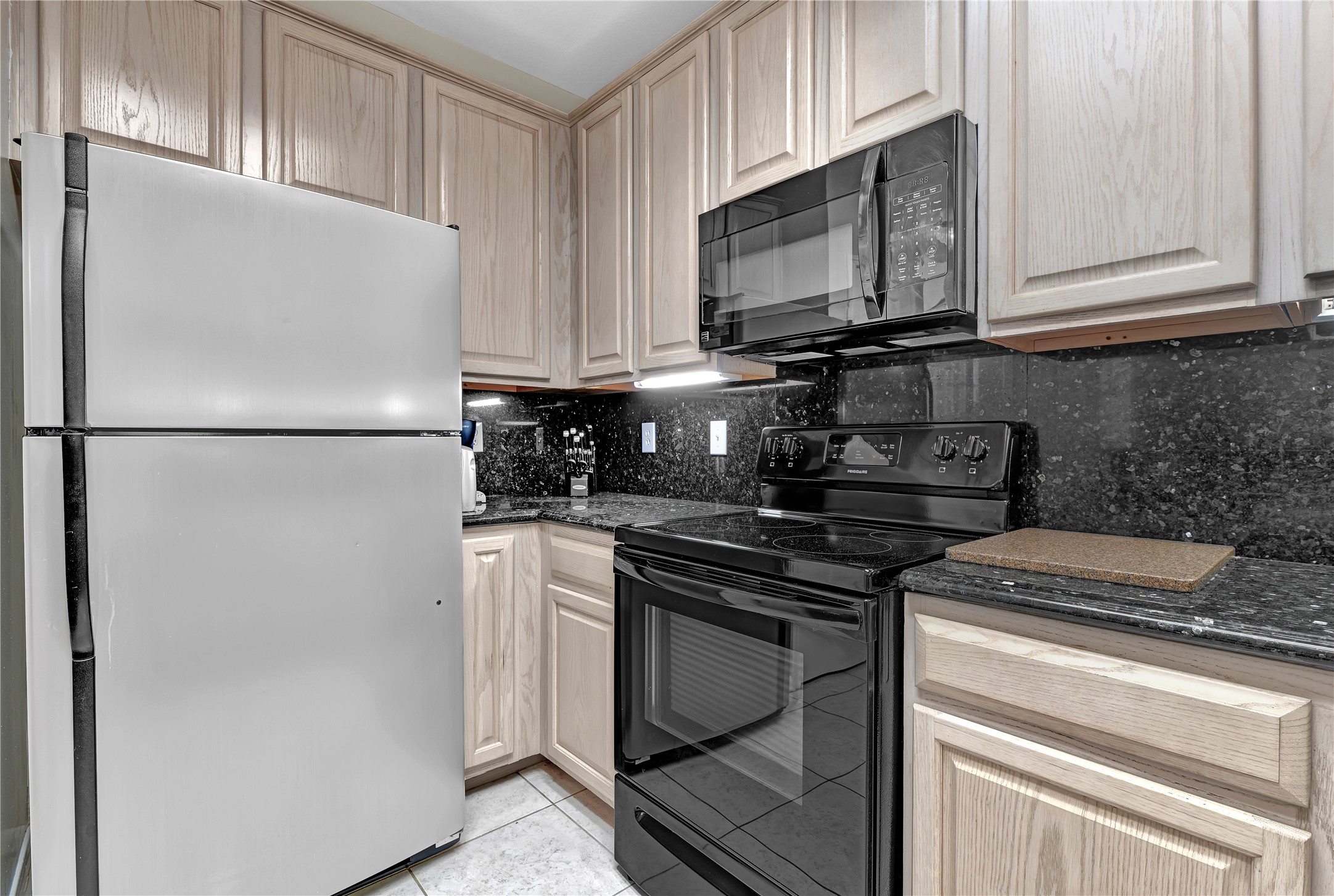 14420 Walters Road, Unit 16 Houston, TX 77014 - Photo 4 of 27 Modern kitchen with stainless steel appliances, black granite countertops, light wood cabinetry, and a tile floor. Cozy and functional layout.