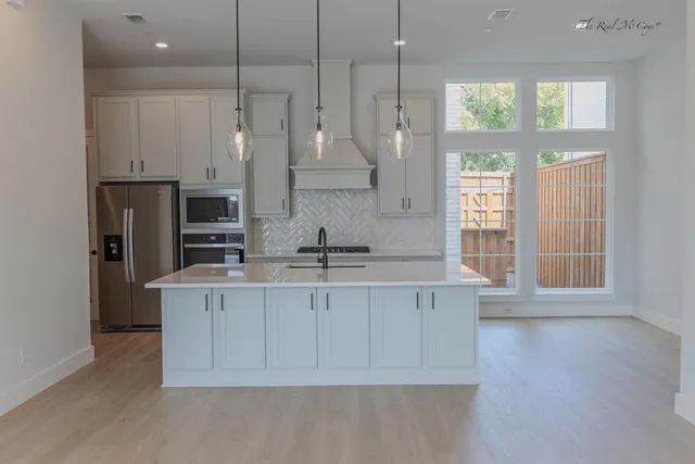 a large kitchen with stainless steel appliances granite countertop a stove a sink a refrigerator white cabinets and wooden floor