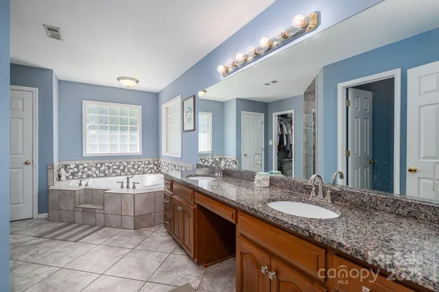 a spacious bathroom with a granite countertop double vanity sink a mirror and a bathtub