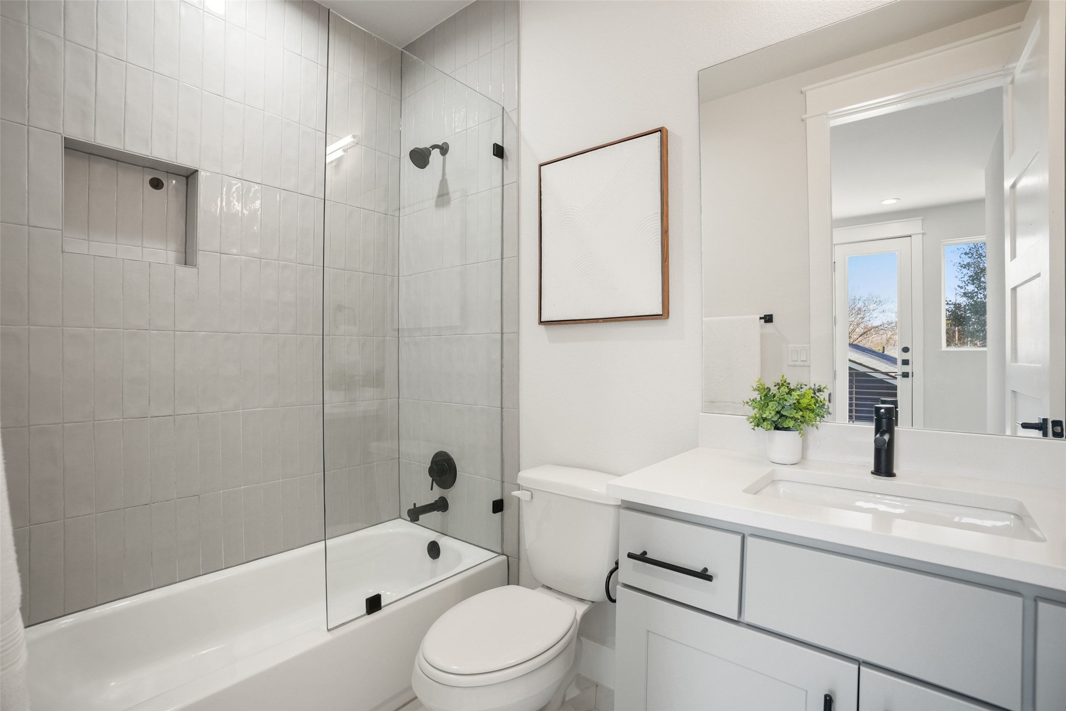 5109 Stone Gate Drive, Unit 2 Austin, TX 78721 - Photo 22 of 36 Bathroom featuring a white bathtub, glass shower partition, wall-mounted matte black shower hardware, and tiled shower surround with an integrated niche