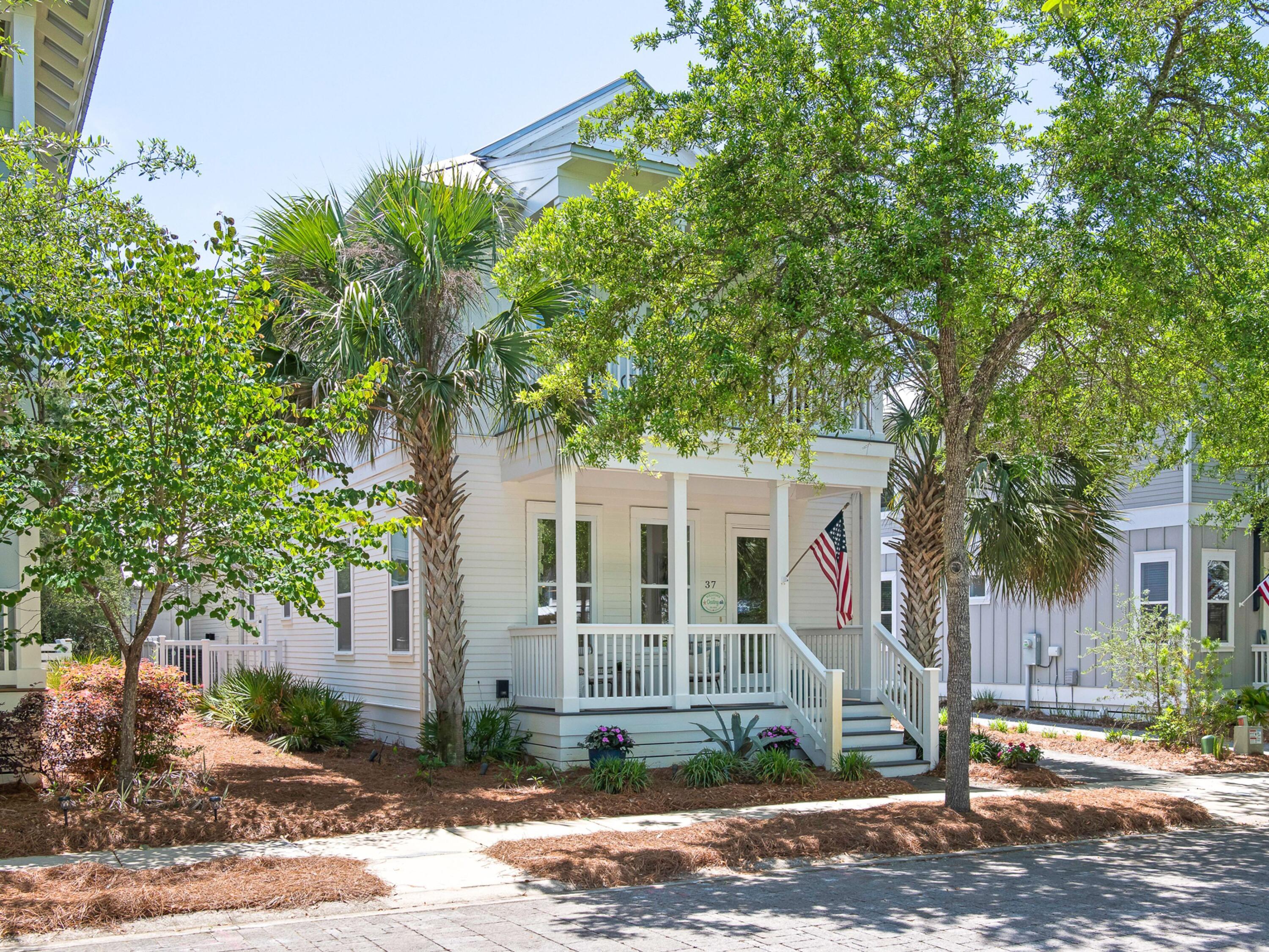 a view of a white house next to a yard with large trees