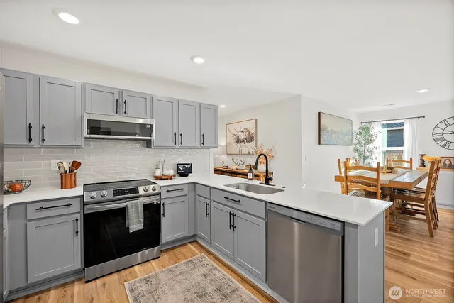 a kitchen with stainless steel appliances granite countertop a stove top oven a sink dishwasher and white cabinets with wooden floor