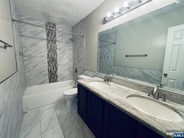 a bathroom with a granite countertop sink toilet mirror and bathtub