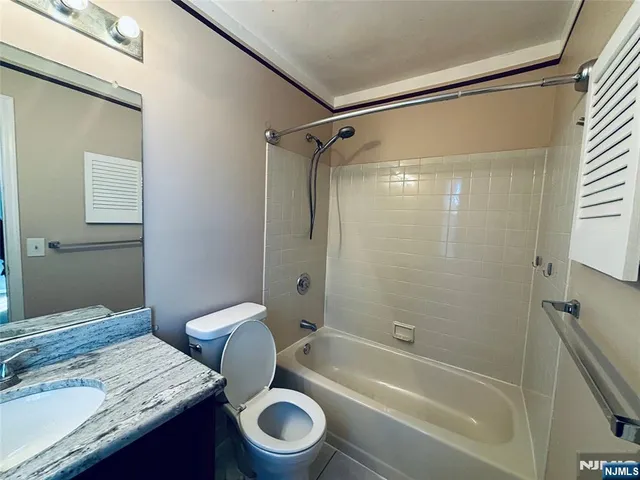 a bathroom with a granite countertop bathtub shower sink vanity and toilet