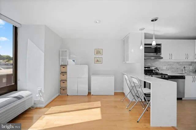 a kitchen with stainless steel appliances kitchen island granite countertop a refrigerator a stove a sink and white cabinets with wooden floor