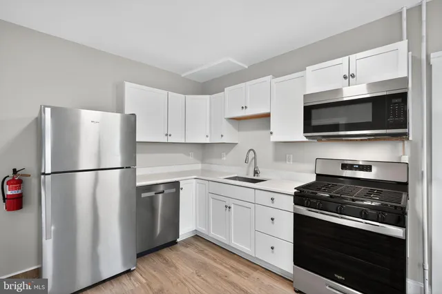 a white kitchen with stainless steel appliances a refrigerator a stove top oven a sink and cabinets