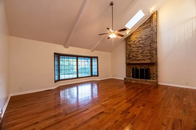 a view of an empty room with wooden floor fireplace and a window