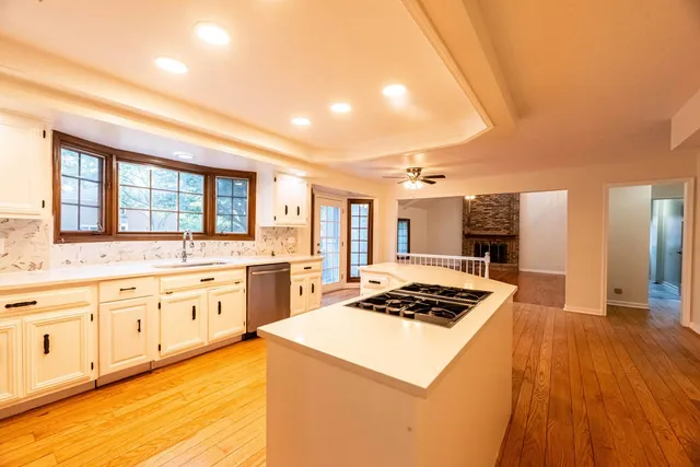 a kitchen with stainless steel appliances kitchen island granite countertop a stove a sink dishwasher and white cabinets with wooden floor