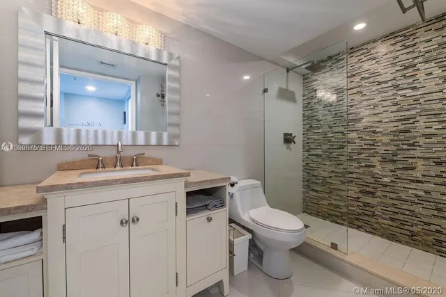 a bathroom with a granite countertop toilet a sink a mirror and a shower