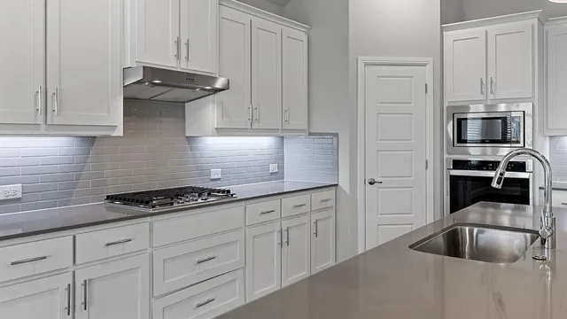 a kitchen with stainless steel appliances granite countertop a sink a stove and white cabinets with wooden floor