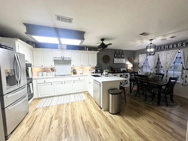 a kitchen with a refrigerator a microwave oven a sink dishwasher and white cabinets with wooden floor