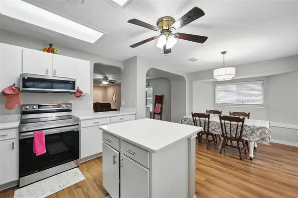 a large kitchen with stainless steel appliances a stove a microwave oven a dining table and chairs with wooden floor