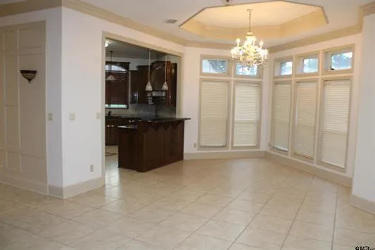 an empty room with chandelier fan and kitchen view